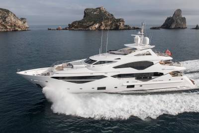 A sleek white yacht cuts through the dark blue ocean, leaving a foamy wake against a backdrop of rugged islands.