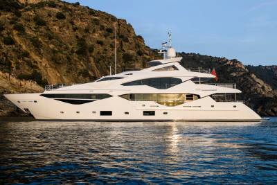 A luxurious white yacht glides serenely on calm blue waters near a rugged, sun-drenched coastline.
