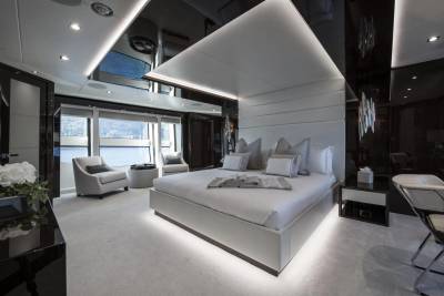 Luxurious yacht bedroom features a king-sized bed, plush seating, and stunning waterfront views through panoramic windows.