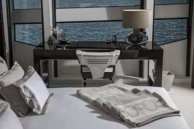 A modern desk with a stylish lamp and decorative items overlooks the tranquil ocean from a luxurious bedroom.