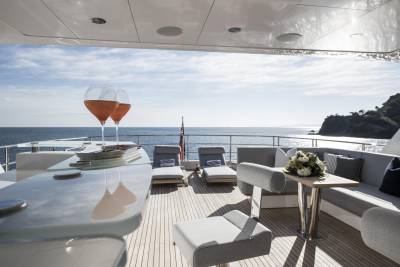 Two glasses of rosé sparkle on a yacht's deck, overlooking a sun-drenched sea and a rocky coastline.