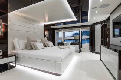 Luxurious yacht bedroom features a plush white bed, modern lighting, and a sleek desk area overlooking the water.