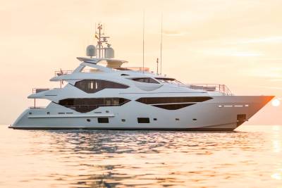 A luxurious white yacht glides across calm waters bathed in the warm glow of a sunset.