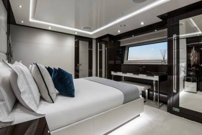 Luxurious yacht bedroom features a plush bed, elegant vanity, and a large window with a serene sky view.