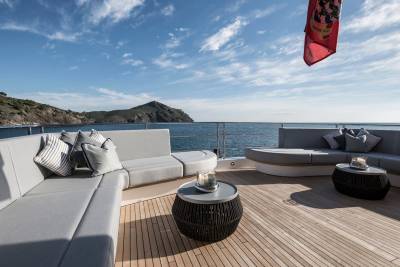 Luxurious outdoor seating on a yacht deck offers a serene view of the Mediterranean coastline under a bright blue sky.
