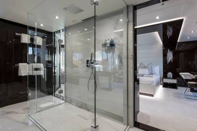 Luxurious yacht interiors feature a sleek, modern bathroom with a glass-enclosed shower and a glimpse into a plush bedroom.