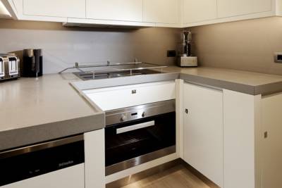 A modern kitchen features sleek white cabinetry, a grey countertop, and stainless steel appliances including a toaster, kettle, and oven.