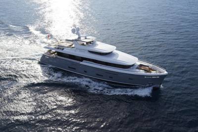 A sleek grey yacht glides through sparkling blue waters, leaving a white wake behind it.