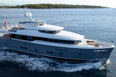 The sleek grey yacht Bijoux glides through the calm blue waters, its white superstructure gleaming under the bright sun.