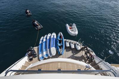 A luxury yacht is equipped with a variety of water toys including jet skis, paddleboards, and an inflatable dinghy.