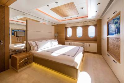 Luxurious yacht cabin features a plush bed, sleek cabinetry, and oval windows offering ocean views.