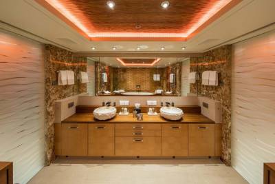 Luxurious bathroom features double vessel sinks, warm wood cabinetry, and a striking textured ceiling with ambient orange lighting.