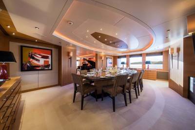 An elegant dining room on a yacht features a grand piano, a beautifully set table, and abstract art.