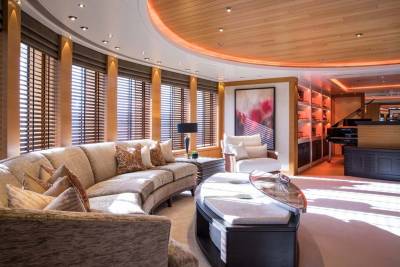 Sunlight streams into this luxurious yacht lounge, illuminating a grand piano, plush seating, and elegant artwork.