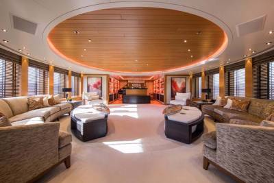 Luxurious seating arrangements surround unique oval ottomans in this opulent yacht lounge with a warm, wood-paneled ceiling.