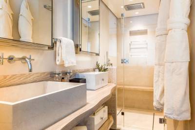 Luxurious white robes hang ready in a modern bathroom featuring sleek marble sinks and a glass-enclosed shower.
