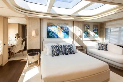 A woman in a robe works at a desk in a luxurious bedroom with a skylight, modern art, and a plush sofa.