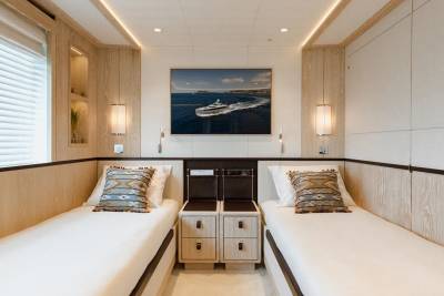 Twin beds with patterned pillows are neatly made in this elegant yacht cabin, illuminated by soft wall sconces.