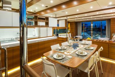 A beautifully appointed dining table awaits guests on this luxurious yacht, set against a backdrop of polished wood and expansive windows.