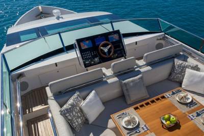 A luxurious yacht deck is set for dining with elegant place settings and comfortable seating overlooking the sparkling blue ocean.