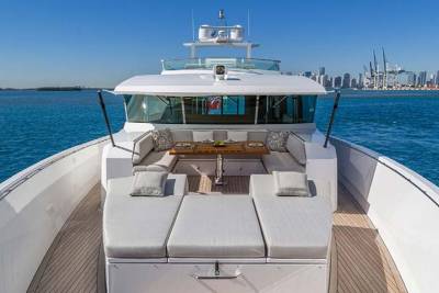 Relax on the spacious deck of this luxurious yacht, complete with plush seating and a dining area, overlooking a distant city skyline.