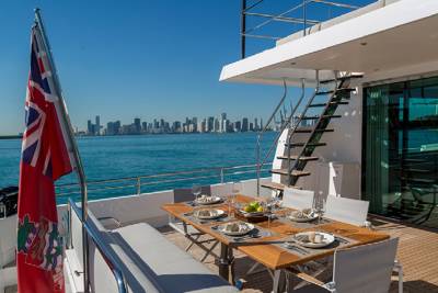 A beautifully set outdoor dining table awaits guests on a luxury yacht with a city skyline in the distance.