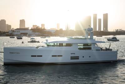 A sleek white yacht cruises through sun-drenched waters with a city skyline in the background.