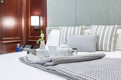 A tray with a tea set and a single white tulip sits on a neatly made bed with decorative pillows.