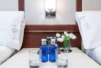 Two beds are prepared with white linens, a vase of tulips, and bottled water on the nightstand.
