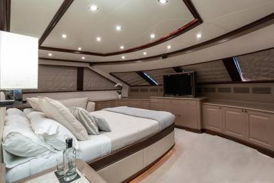 Luxurious yacht cabin features a plush bed, integrated entertainment center, and elegant built-in cabinetry.