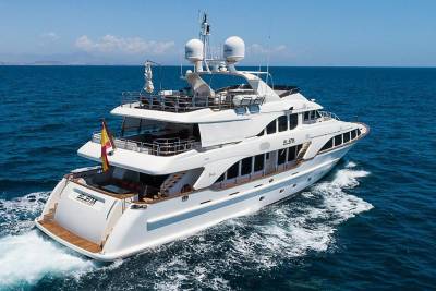 A luxurious white yacht cruises through the sparkling blue ocean under a clear sky.