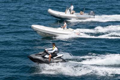 A jet ski cuts through the waves as two inflatable boats speed along the sparkling blue ocean.