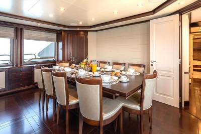 A luxurious dining room aboard a yacht is set for breakfast with a fruit basket, pastries, and coffee.