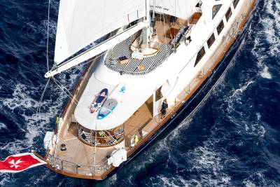 A woman in a dark outfit walks on the deck of a luxurious yacht sailing through the deep blue sea.
