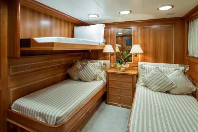 Two cozy beds with striped linens are nestled within the warm wood-paneled cabin of this luxurious yacht.