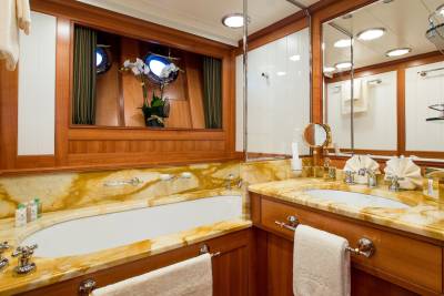 Luxurious yacht bathroom features a marble vanity, a deep soaking tub, and porthole windows offering ocean views.