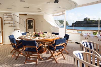 A beautifully set dining table awaits guests on a yacht deck overlooking a picturesque coastal landscape.