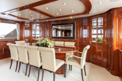 Luxurious yacht dining room features a polished wood table, cream upholstered chairs, and a large mirror reflecting the elegant interior.