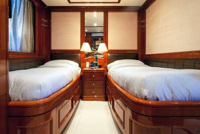 Luxurious twin beds with crisp white linens are nestled within a richly paneled stateroom aboard a yacht.