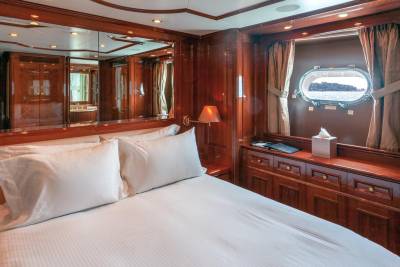 Luxurious wood-paneled stateroom offers a comfortable bed and a porthole view of the sea.