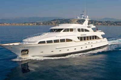 The luxurious yacht Enchantress glides through the azure waters, with a picturesque coastal town nestled in the hills behind.