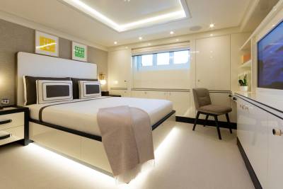 A plush blanket drapes over a modern bed in this luxurious yacht stateroom, illuminated by soft, ambient lighting.