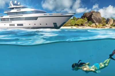 A luxurious yacht anchors near a tropical island while a woman snorkels in the clear blue water below.
