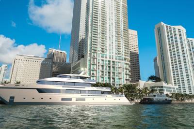 A sleek white yacht docks in a vibrant city harbor, dwarfed by towering modern skyscrapers under a clear blue sky.