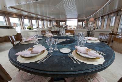 A formal dining table is set with pink napkins and crystal glasses aboard a luxurious yacht.