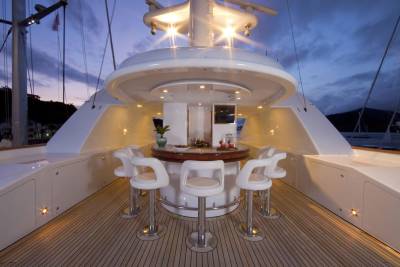 Elegant white bar stools surround a polished wooden bar on a yacht deck as twilight descends.