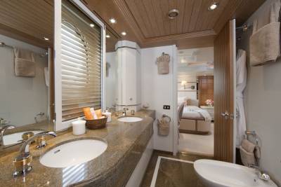 A luxurious yacht bathroom features a granite countertop, dual sinks, and a view into a well-appointed bedroom.