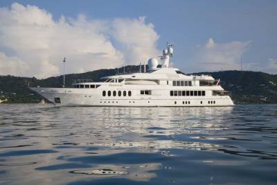 The luxurious yacht Huntress glides serenely across calm waters with a verdant, hilly coastline in the background.