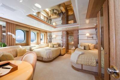 Luxurious yacht stateroom features twin beds, a plush sofa, and serene ocean views through oval windows.