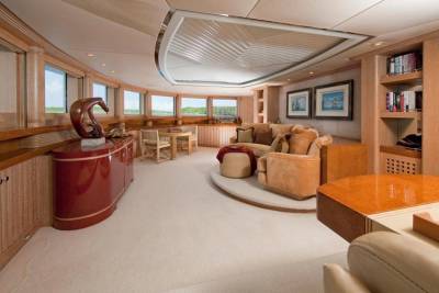 Luxurious yacht interiors feature warm wood tones, plush seating, and expansive windows offering scenic ocean views.